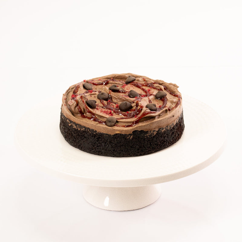 Plant-based chocolate cake topped with glossy raspberry and chocolate buttons.