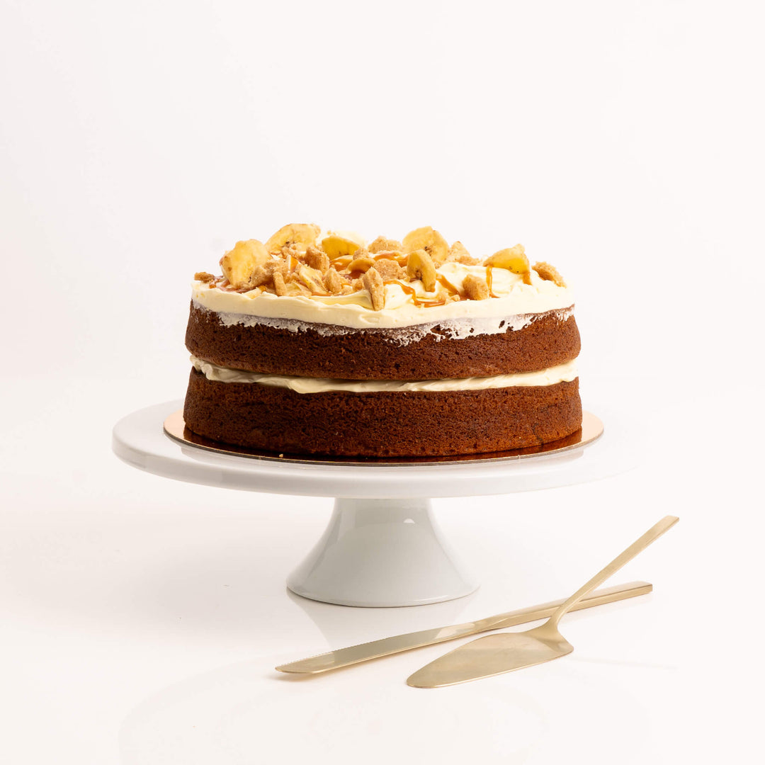 Side view of moist banana cake with cream cheese frosting and caramel drizzle by Sweet Talk, displayed on a cake stand, available for delivery in Auckland.