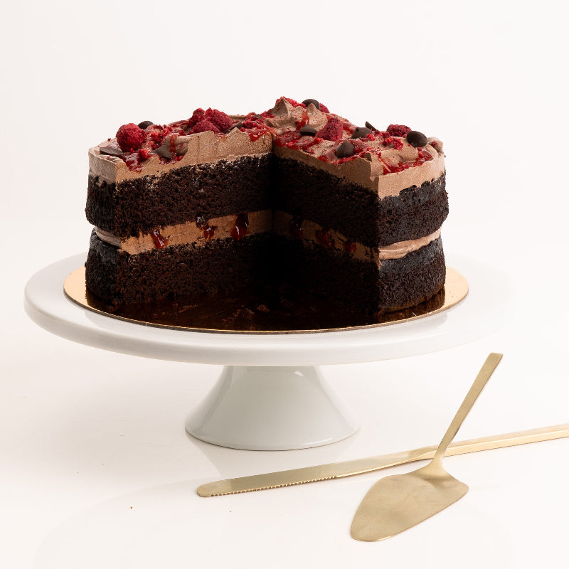 Dark vegan chocolate cake topped with freeze-dried raspberries and couverture buttons.